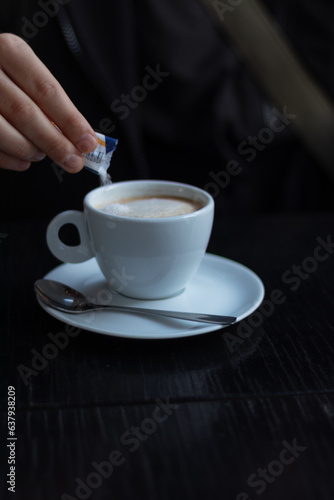 Putting sugar on a cup of coffee on a table 