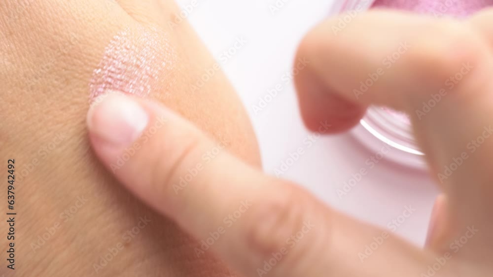 Close up shot of woman applying eyeshadow on hand skin. Eyeshadow smeared with a finger on the hand Close up shot of woman applying eyeshadow on hand skin. Eyeshadow smeared with a finger on the hand