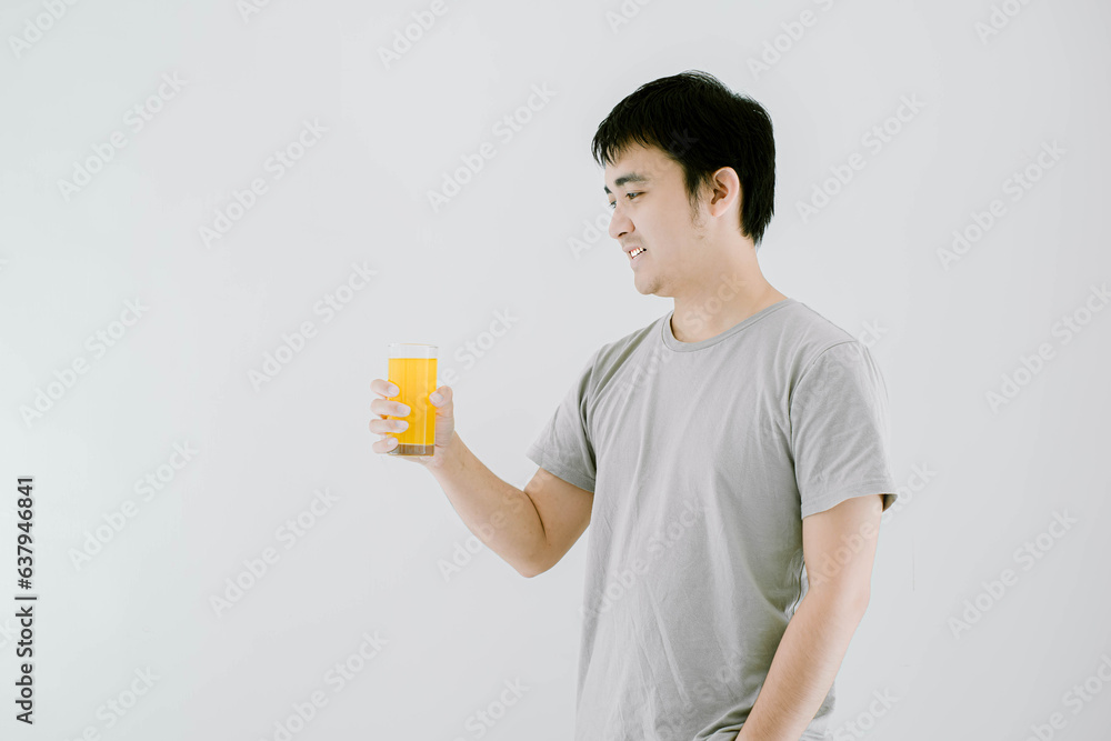 Selective focus shot of a young Asian man holding a glass of vitamin c water and smiling while looking at it. Isolated white background.