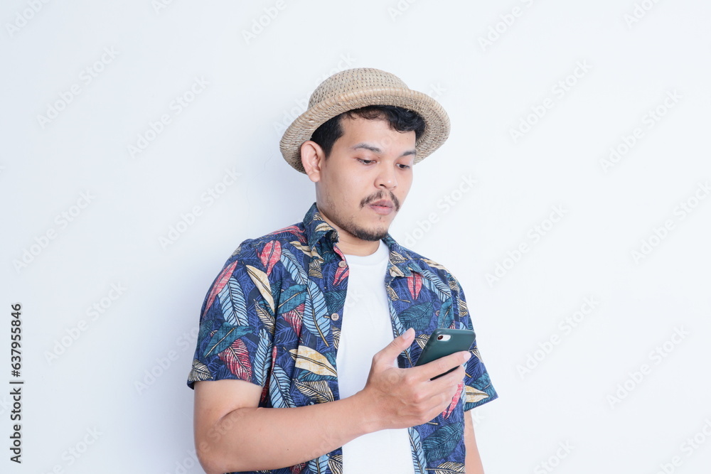 Young asian man wearing beach shirt showing confused face while holding a mobile phone Young asian man wearing beach shirt showing confused face while holding a mobile phone