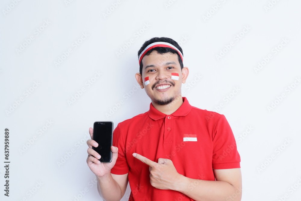 A portrait of a smiling Asian man wearing headband and showing his phone, isolated by white background. Indonesia's independence day concept A portrait of a smiling Asian man wearing headband and showing his phone, isolated by white background. Indonesia's independence day concept