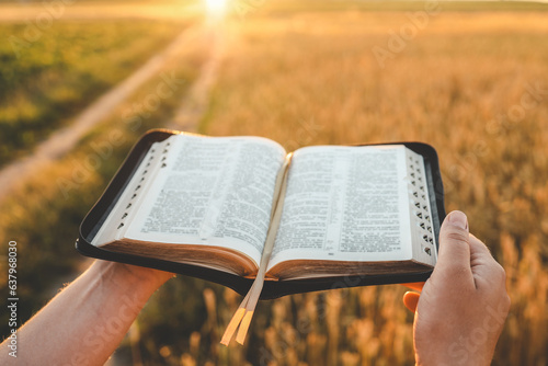 Foto Open bible in hands, wheat field and road, christian concept