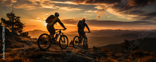 Cyclists silhouette standing on big rock against sunset 