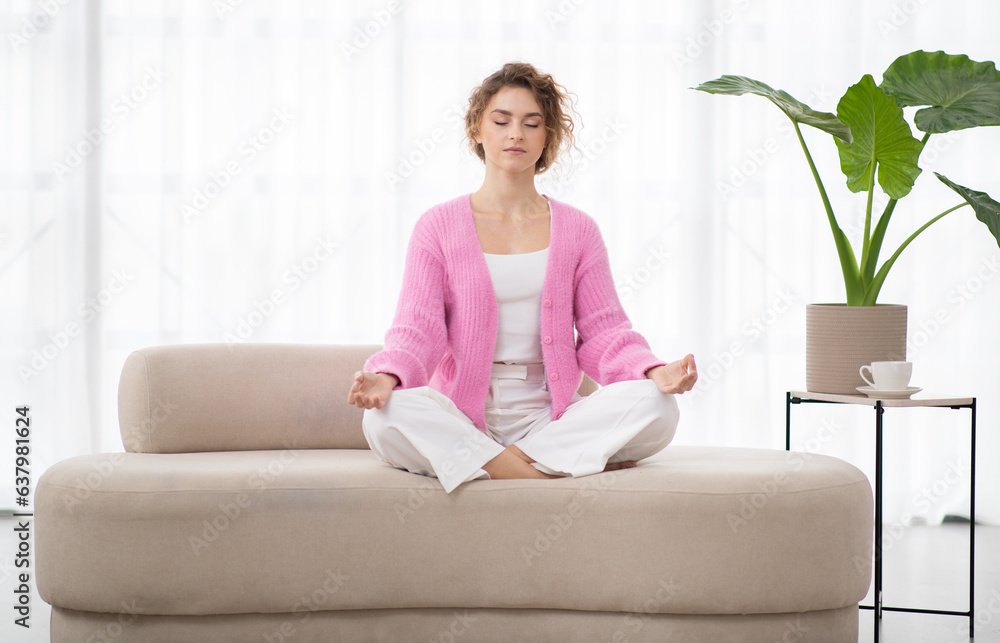 Calm young woman sitting on couch, meditating with closed eyes at home Calm young woman sitting on couch, meditating with closed eyes at home