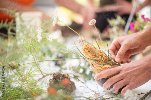 Detail of hands making flower arrangement, outdoor ikebana workshop, different flower arrangements in progress.