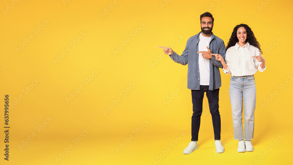 Happy Middle Eastern Spouses Pointing Aside Over Yellow Background, Panorama