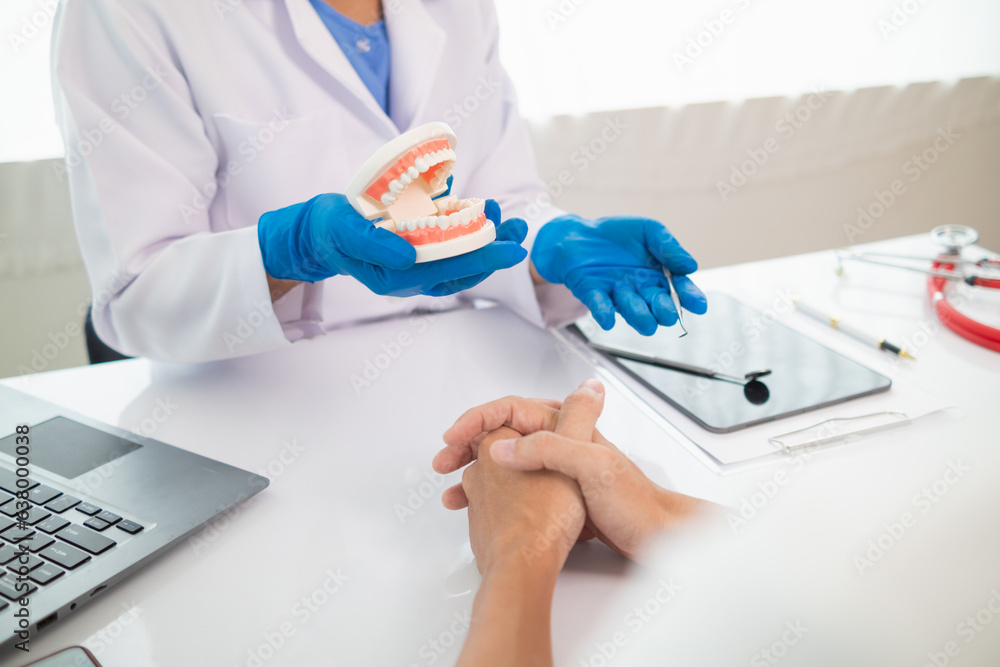 The dentist holds a denture in his hand and shows the patient the position of the problem tooth and the dentist explains how to treat the tooth for the patient to understand. Copy space for text The dentist holds a denture in his hand and shows the patient the position of the problem tooth and the dentist explains how to treat the tooth for the patient to understand. Copy space for text