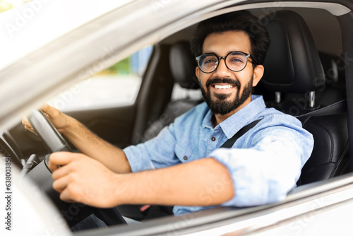 Happy eastern guy driving white auto, smiling at camera © Prostock-studio