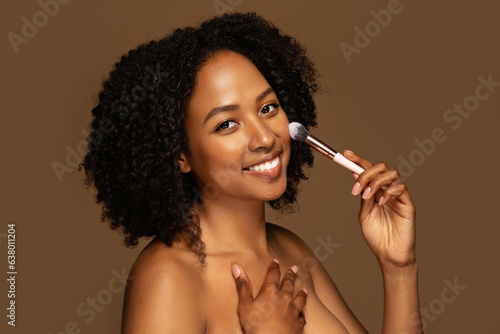 Cheerful pretty half-naked young black woman holding makeup brush