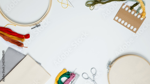 Embroidery set fot stitching. Beige cotton cloth in embroidery hoop on white background with fabric, colorful threads, scissors and needls. Indoor hobby concept with copy space, top view