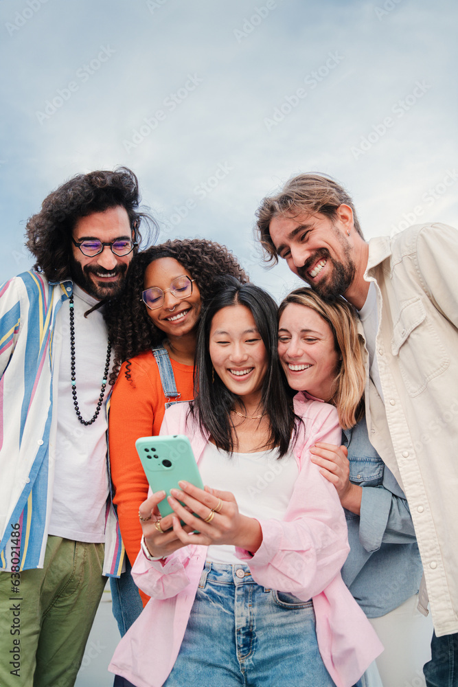 Vertical portrait of a multiracial group of young adult friends enjoying and smiling using a mobile phone app. Diverse buddies having fun watching and sharing on the social media with a cellphone Vertical portrait of a multiracial group of young adult friends enjoying and smiling using a mobile phone app. Diverse buddies having fun watching and sharing on the social media with a cellphone