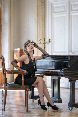 A girl in a twenties outfit sits on a chair at an antique black piano