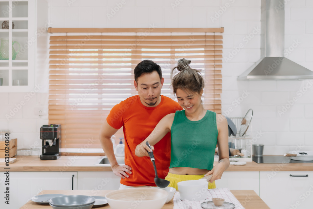 Husband looking at wife who cooking lunch for him. Happy asian couple in kitchen Husband looking at wife who cooking lunch for him. Happy asian couple in kitchen