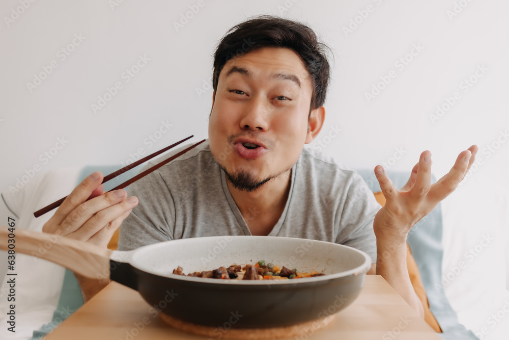 Happy funny face of asian man eating homemade food in the pan with chopsticks.