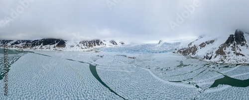 Panoramic drone view of the islands with the snowy mountains of Svalbard archipelago and the breaking ice rig of the frozen Arctic Ocean.