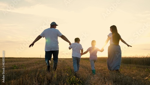 Happy farmers family with children runs through wheat field at sunset. Big family, group of people in nature. Son, daughter, dad, mom, walk hand in hand in outdoors. Child dream, complete family, kids