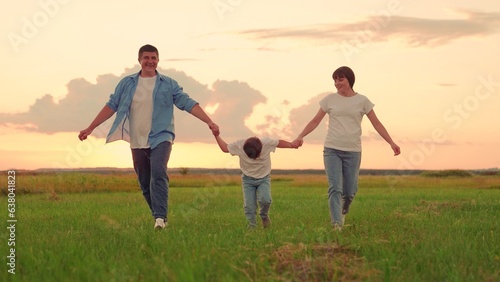 Family, Kid, run on green grass in meadow. Mother, father, child dream together in park at sunset. Happy family, child, walk through summer field, holding hands. Mom dad son walks together in nature