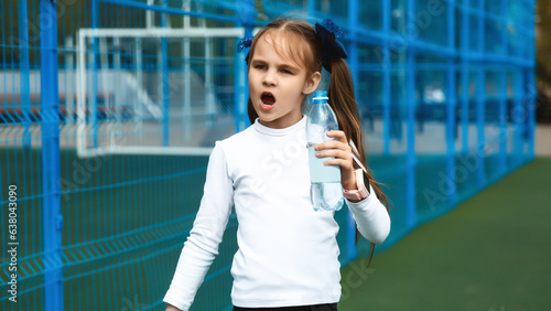 Obraz na plátne Portrait of a cute little girl holding a bottle of water while playing in an out