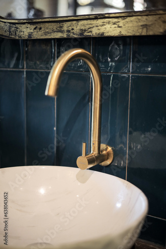 Vintage style old bathroom interior with white round ceramic sink with gold brass faucet on top of old wooden cabinet, stone wall background