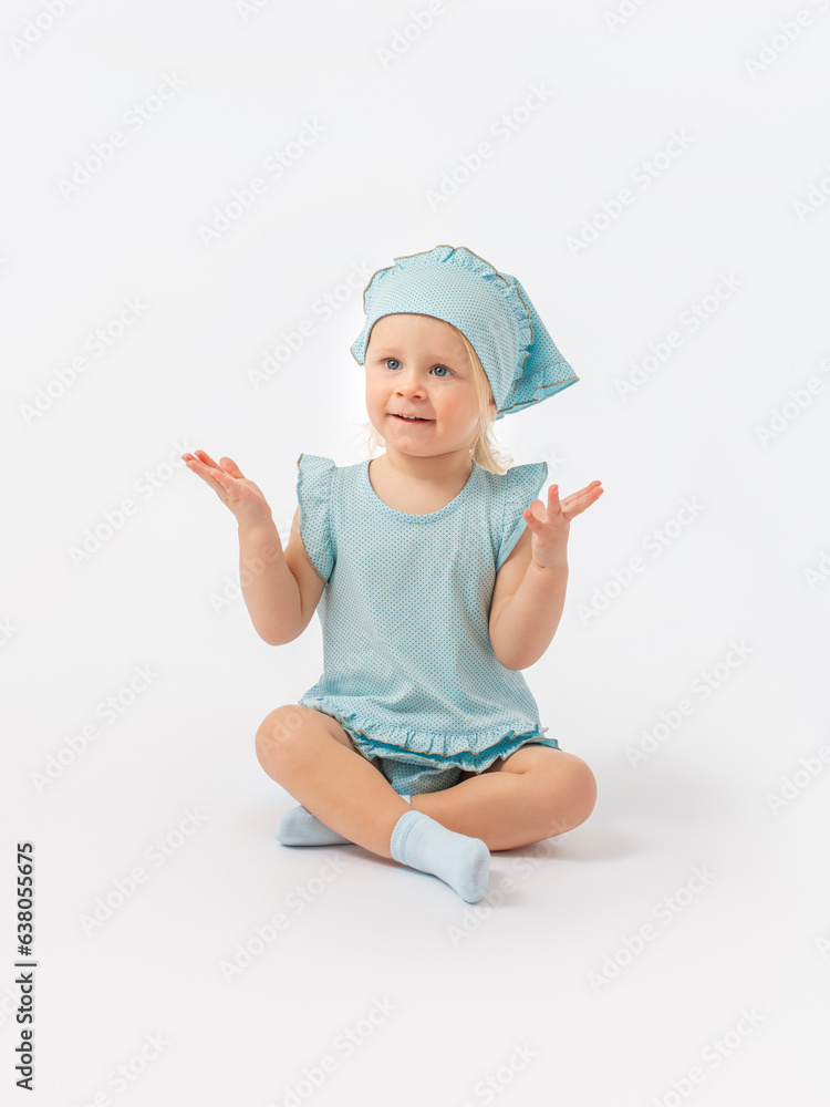 Learning, playing. A 2-year-old toddler girl in a kerchief is sitting on the floor, counting her fingers, legs crossed in socks on a white background.
