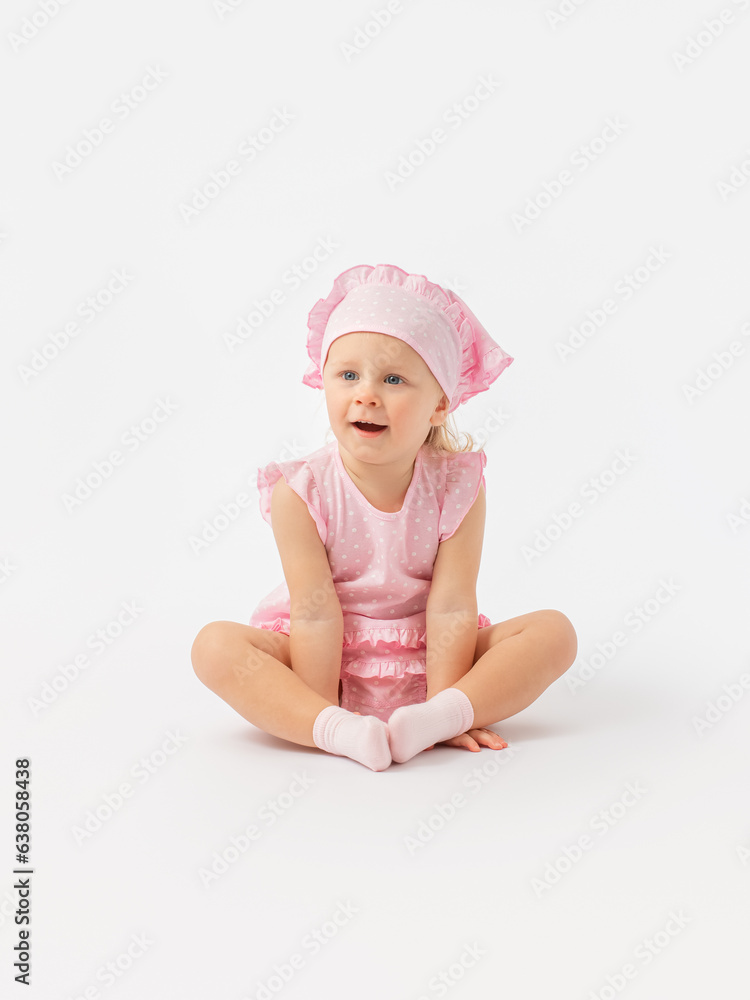 Surprise, a little girl 2 years old in a pink dress and a scarf sits on the floor and looks carefully with her mouth open. Surprise, a little girl 2 years old in a pink dress and a scarf sits on the floor and looks carefully with her mouth open.