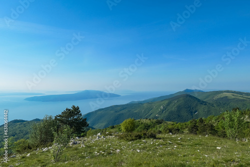 A panoramic view on the Mediterranean Sea in Croatia from Vojak. The mountain is overgrown with lush green plants. Few islands in the back. Early morning hiking by the sea. Clear, blue sky. Remedy