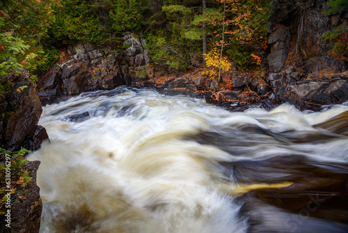 Fast flowing water at the top of a waterfall along a river running through a forest in autumn photo