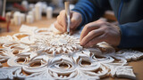 A close-up of hands crafting a delicate snowflake from paper, surrounded by an array of intricately cut designs.  