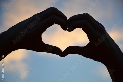 female hands folded the shape of a heart against the sky at sunset or dawn. a symbol of love  fidelity  sympathy and recognition of feelings. silhouette against the background of sunset or dawn