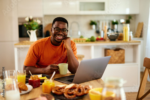 African American man using laptop while enjoying breakfast  at home