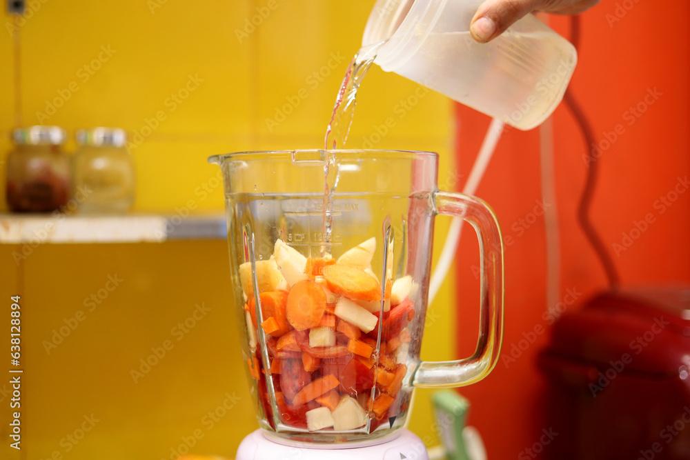 male hand pouring water into blender. blend fruit. make fruit juice
