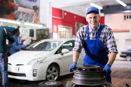 Experienced mechanician changing car wheel and tire of modern car in auto repair shop photo