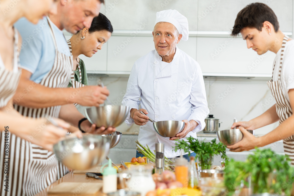 Smiling elderly man, seasoned professional chef conducting culinary courses, imparting cooking skills to diverse group of people of different ages