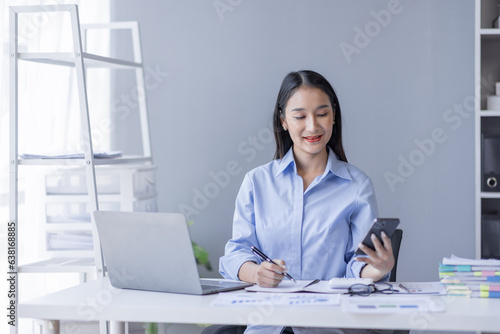 Business Asian woman working at office with phone on documents at her desk, doing planning analyzing the financial report, business plan investment, finance analysis concept 