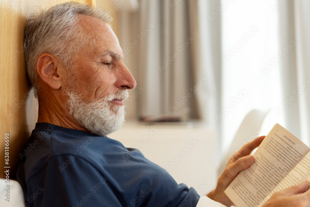 Fototapeta premium Closeup, handsome, serious senior man reading book, lying in bed, morning routine