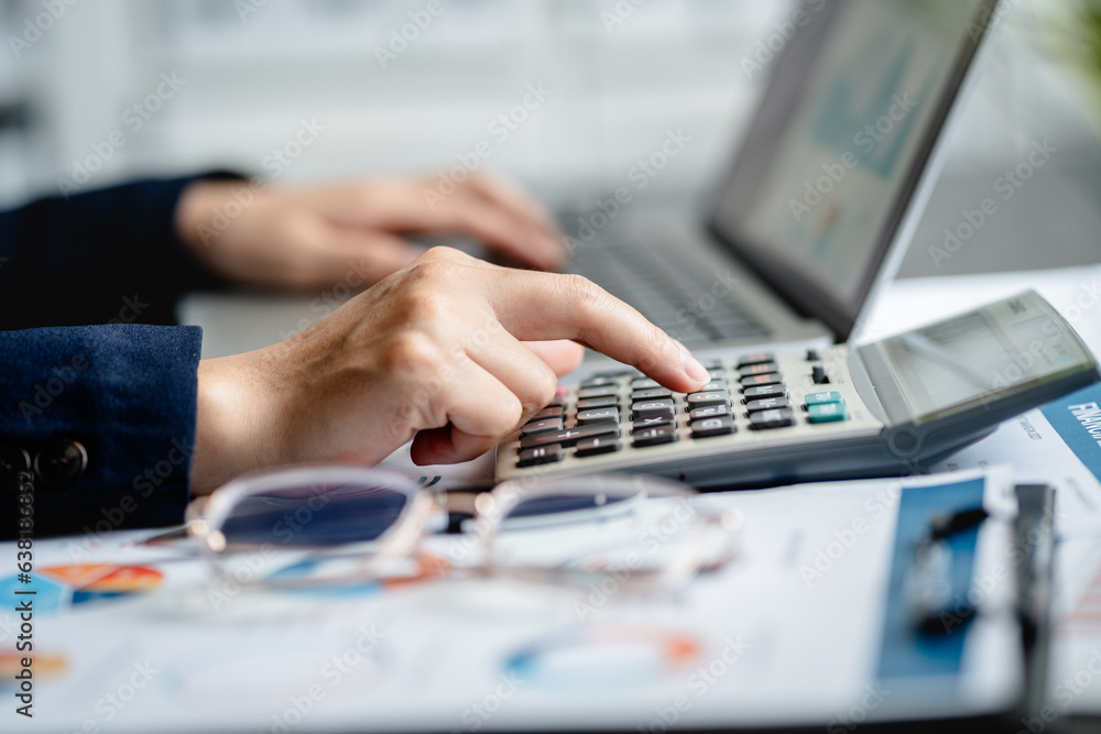 Close up view of Businesswomen or Accountants using calculator and a laptop computer to analyze business report graphs and finance charts at the workplace, financial and investment concept. Close up view of Businesswomen or Accountants using calculator and a laptop computer to analyze business report graphs and finance charts at the workplace, financial and investment concept.