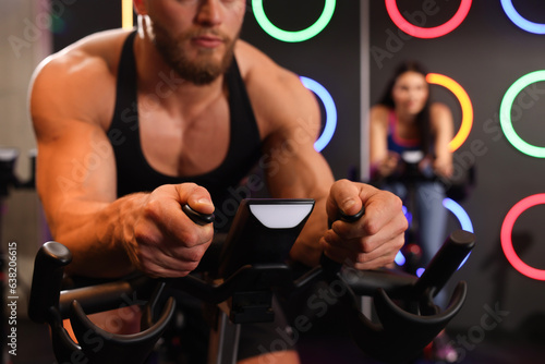 Young man training on exercise bike in fitness club, closeup