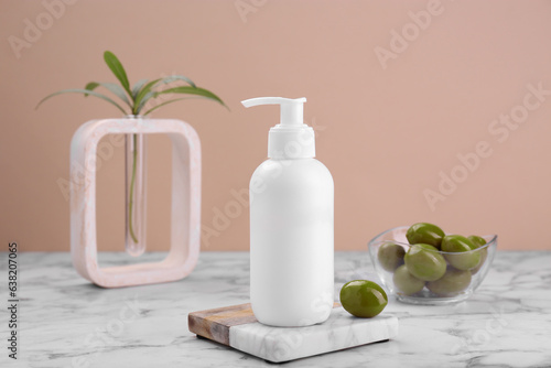 Bottle of cosmetic product with olive essential oil on white marble table