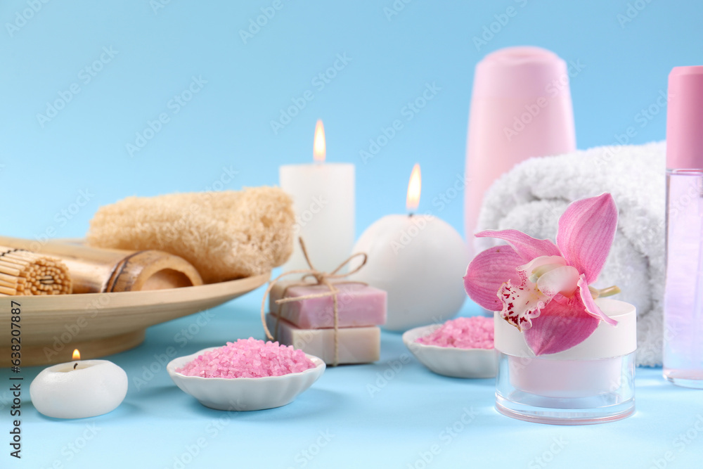 Retreat concept. Composition with different spa products, burning candles and beautiful orchid on light blue background
