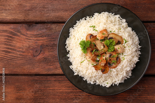 Delicious rice with mushrooms and parsley on wooden table, top view. Space for text