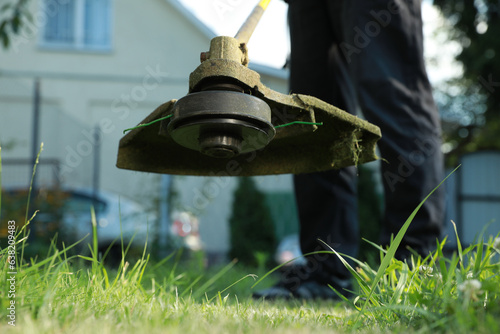 Man cutting green grass with string trimmer outdoors, closeup photo