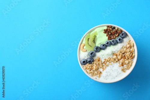 Tasty smoothie bowl with fresh kiwi fruit  blueberries and oatmeal on light blue background  top view. Space for text