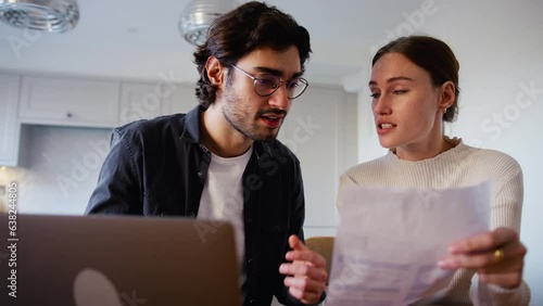 Worried young couple at home arguing looking at laptop in kitchen counter worried about bills and cost of living crisis - shot in slow motion photo