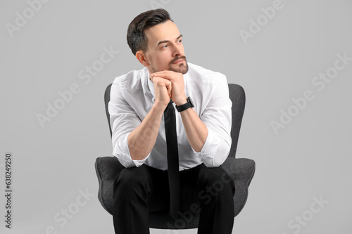 Handsome businessman sitting in armchair on grey background © Pixel-Shot
