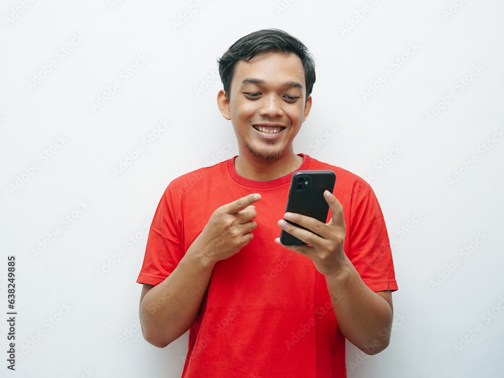 Portrait of young Asian Indonesian smiling while other hand finger pointing smartphone. Red t-shirt for 17 august indonesia independence day concept Portrait of young Asian Indonesian smiling while other hand finger pointing smartphone. Red t-shirt for 17 august indonesia independence day concept