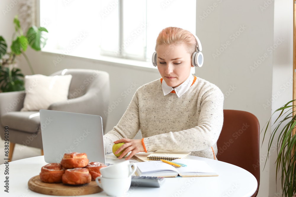 Female student in headphones studying with laptop at home
