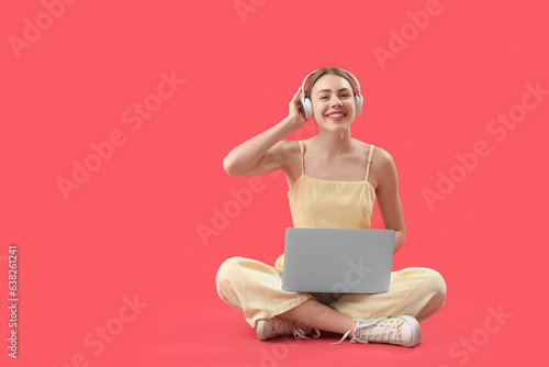 Female programmer in headphones with laptop sitting on red background
