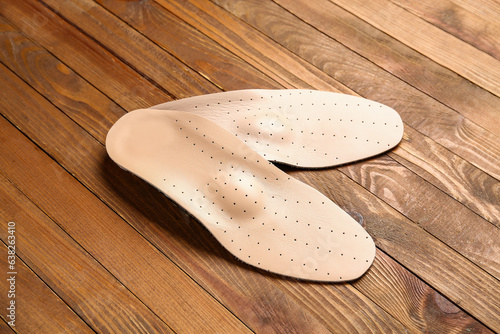 Pair of leather orthopedic insoles on wooden background