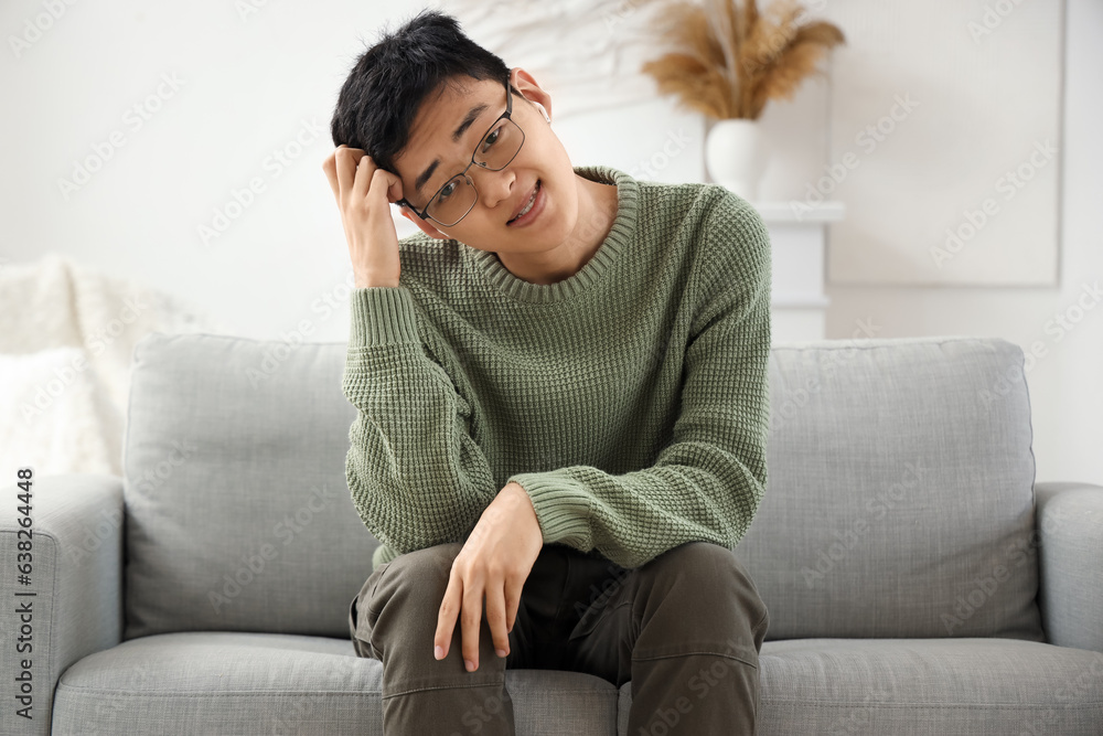 Upset young Asian man in earphones video chatting on sofa at home Upset young Asian man in earphones video chatting on sofa at home