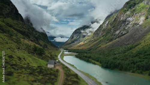 A road winds along the river through the green Norwegian valley. Aerial view, pan forward. photo